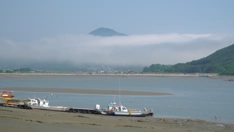 Fisher's-boats-stuck-in-the-mud-on-low-tide-at-Ganghwado-island-in-South-Korea,-haze-and-vapor-over-mountain-peaks