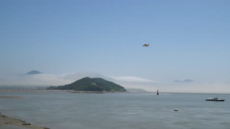 Fisherman's-ship-in-the-Yellow-sea-on-low-tide,-Red-navigational-buoy-floating-in-between-islands,-a-mountain-covered-in-dense-mist,-Ganghwado-island,-South-Korea,-static-wide