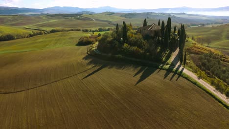Beautiful-landscape-scenery-of-Tuscany-in-Italy---farmhouse,-cypress-trees-along-white-road---aerial-view