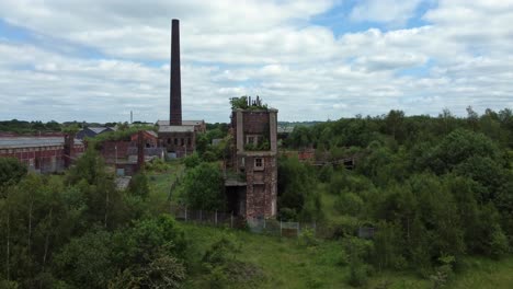 Abandoned-old-overgrown-coal-mine-industrial-rusting-pit-wheel-buildings-aerial-view-rising-front-shot