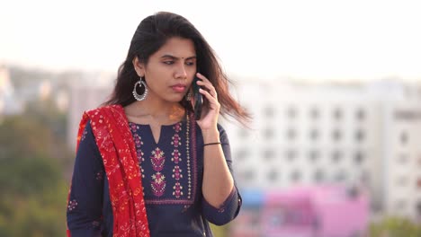 Schöne-Indische-Frau-In-Einem-Sari,-Der-Ihr-Handy-Benutzt-Und-Lächelnd-Auf-Einem-Balkon-Steht,-Mit-Der-Stadt-Reflektiert