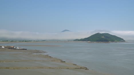 Fisher-ships-stuck-in-the-mud-on-low-tide-at-Ganghwado-island-in-South-Korea,-haze-and-vapor-over-mountain-peaks