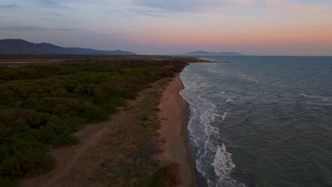 Cinematic-high-altitude-aerial-drone-footage-above-a-sandy-sunset-beach-at-the-seaside-near-Castiglione-in-the-iconic-Maremma-nature-park-in-Tuscany,-Italy,-with-waves,-islands-and-a-dramatic-red-sky