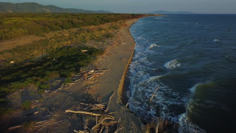 Cinematic-aerial-drone-footage-flying-forwards-above-a-sandy-sunrise-beach-at-the-seaside-near-Alberese-in-the-iconic-Maremma-nature-park-in-Tuscany,-Italy,-with-waves,-islands-and-a-dramatic-red-sky