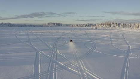 Aerial-drone-shot-of-snowmobiler-driving-fast-on-deep-snow-field