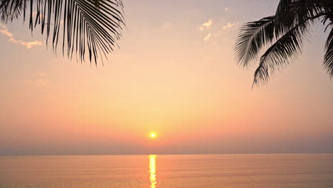 A-dramatic-orange,-pink-and-yellow-sunsetover-the-ocean-horizon-is-framed-by-palm-fronds