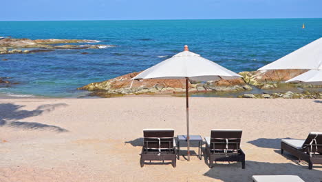Deckchairs-Under-Parasol-In-Tropical-Beach-rocky-beach-in-Marmaris,-Turkey-on-a-sunny-day