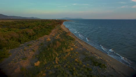 Cinematic-high-altitude-aerial-drone-footage-above-a-sandy-sunset-beach-at-the-blue-seaside-near-Castiglione-in-the-iconic-Maremma-nature-park-in-Tuscany,-Italy-with-waves,-islands-and-a-dramatic-sky