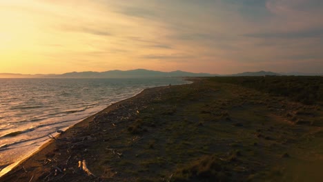 Epic-cinematic-aerial-drone-footage-of-the-sunset-above-a-sandy-beach-at-the-seaside-near-Alberese-in-the-iconic-Maremma-nature-park-in-Tuscany,-Italy,-with-waves,-islands-and-a-dramatic-red-sky