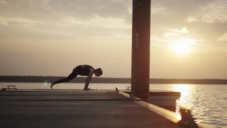 Young-woman-doing-dynamic-yoga-flow-on-jetty-at-sunset,-slow-motion