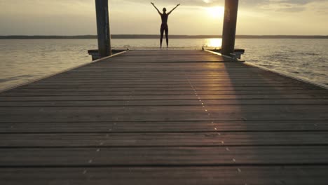 Young-woman-doing-yoga-while-standing-on-jetty-at-sunset,-slow-motion