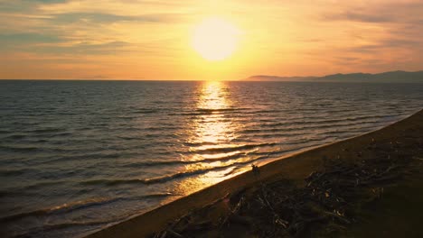 Cinematic-backwards-aerial-drone-footage-of-the-sunset-at-a-sandy-beach-at-the-seaside-near-Alberese-in-the-iconic-Maremma-nature-park-in-Tuscany,-Italy,-with-waves,-islands-and-a-dramatic-red-sky
