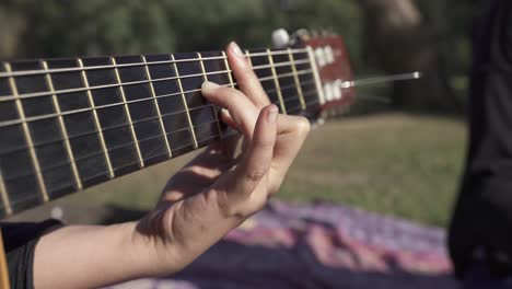 Close-up-shot-of-young-woman-playing-guitar-outdoors,relaxing-in-park-during-sunny-day