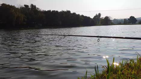 A-fishing-rod-viewed-from-the-side-overlooking-a-pond-with-the-sunlight-reflecting-off-the-water