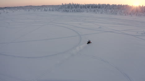 Drone-shot-of-a-fast-snowmobile-rides-towards-the-sunset-and-forest-during-a-cold-winter-season-in-Sweden
