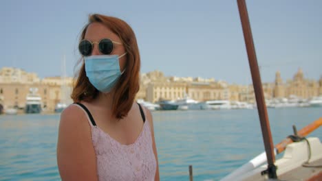 Mujer-Turista-Con-Mascarilla-Disfrutando-De-Un-Paseo-En-Bote-En-Un-Clima-Ventoso-En-El-Puerto-Maltés,-Malta---Toma-De-Mano-De-4k