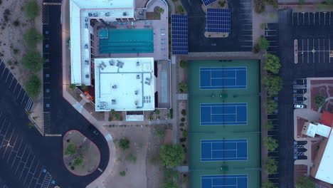 Top-View-Of-Tennis-Courts-And-Swimming-Pool-In-A-Sports-Facility-With-Solar-Paneled-Roofs