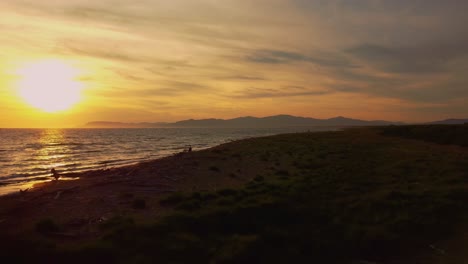 Cinematic-aerial-drone-footage-of-the-sunset-at-a-sandy-beach-at-the-seaside-near-Alberese-in-the-iconic-Maremma-nature-park-in-Tuscany,-Italy,-with-waves,-islands-and-a-dramatic-red-sky