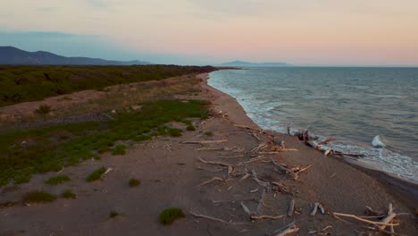 Epic-cinematic-high-altitude-aerial-drone-footage-above-a-sandy-sunset-beach-at-the-seaside-near-Alberese-in-the-iconic-Maremma-nature-park-in-Tuscany,-Italy-with-waves,-islands-and-a-dramatic-red-sky