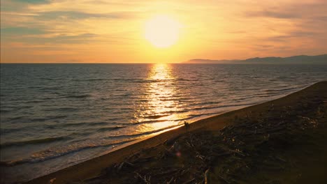 Epic-cinematic-aerial-drone-footage-of-the-sunset-at-a-sandy-beach-at-the-seaside-near-Alberese-in-the-iconic-Maremma-nature-park-in-Tuscany,-Italy,-with-waves,-islands-and-a-dramatic-red-sky