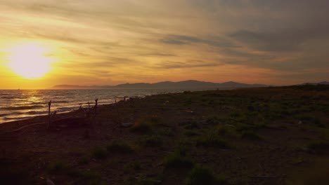 Slow-cinematic-low-aerial-drone-footage-of-the-sunset-at-a-sandy-beach-at-the-seaside-near-Alberese-in-the-iconic-Maremma-nature-park-in-Tuscany,-Italy,-with-waves,-islands-and-a-dramatic-red-sky