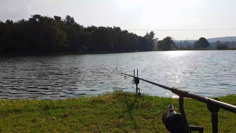 A-fishing-rod-waiting-for-a-bite-with-the-sun-setting-over-a-calm-lake-in-the-distance