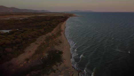 Epic-high-altitude-aerial-drone-footage-above-a-sandy-sunset-beach-at-the-seaside-near-Castiglione-in-the-iconic-Maremma-nature-park-in-Tuscany,-Italy,-with-waves,-islands-and-a-dramatic-red-sky