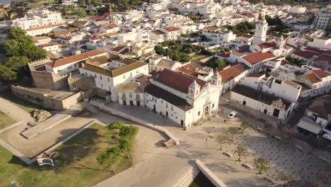 Aerial-of-the-old-church-and-castle-in-Lagos,-Portugal-while-a-white-bird-flies-arises
