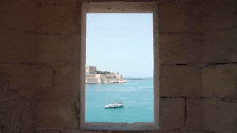 Medieval-city-view-with-sea-coast-and-tourist-boat-through-window-frame---static-shot