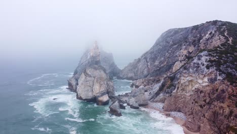 Ascending-Shot-of-a-Moody,-Foggy-Beach-at-Praia-da-Ursa,-Portugal