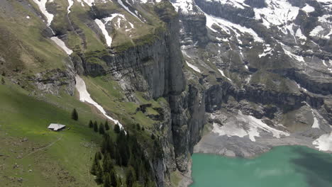 Lonely-alm-sitting-on-the-verge-of-a-steep-cliff-overlooking-the-Oeschinensee-in-Switzerland