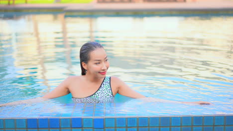 Asian-young-woman-leaning-on-the-border-inside-swimming-pool-smiling,---front-view-daytime-elevated-view,-template-copy-space
