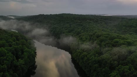 Narrow-river-surrounded-by-dense-forest-and-rising-fog,-early-morning-view