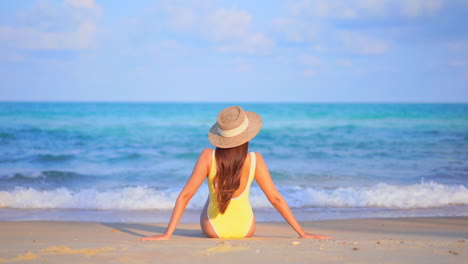 Unrecognizable-woman-in-yellow-swimwear-sitting-on-white-sand-beach-in-front-of-the-sea