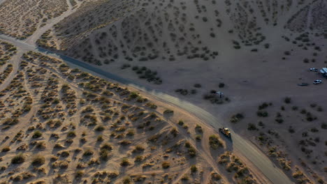A-tow-truck-drives-along-a-dusty-desert-road-at-sunset-with-long-shadows---pull-back-follow-aerial-view
