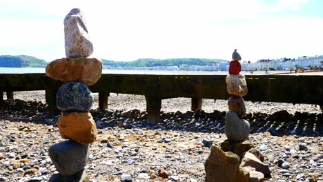 Colourful-rocks-arrangement-balanced-on-sunny-Llandudno-beach-seaside-promenade-shoreline-dolly-left