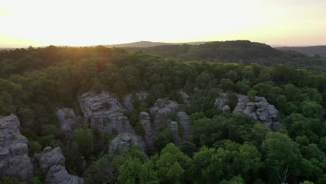 Forest-growing-over-rocky-cliff-with-majestic-sunrise,-aerial-view