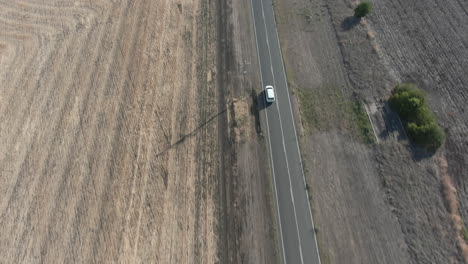 Aerial-top-down-shot-following-a-vehicle-on-the-road-tilts-up-to-reveal-a-barren-drought-affected-landscape-of-farmland-and-fields,-in-Stanthorpe-Australia