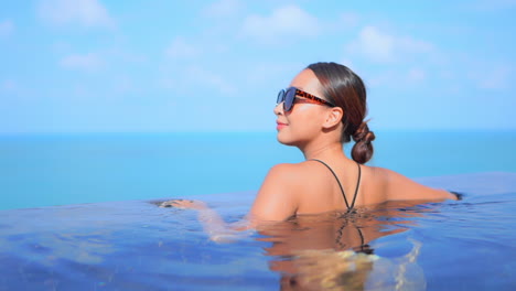 Back-of-attractive-woman-learning-on-the-edge-of-infinity-pool-with-stunning-view-of-open-seascape-on-background,---sunny-day-slow-motion