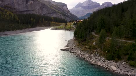 Aerial-view-of-Mountains,-fall-forest-and-sun-reflection-at-Turquoise-glacier-lake-Oeschinensee
