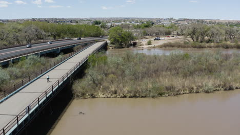 Person,-Die-Mit-Dem-Fahrrad-Auf-Der-Straßenbrücke-über-Den-Fluss-Rio-Grande-Von-Albuqurque,-New-Mexico,-Fährt---Antenne
