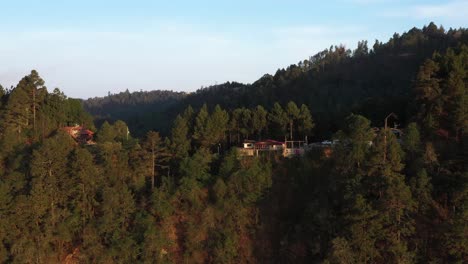 Vista-Aérea-De-Edificios-Y-Casas-En-La-Cima-De-Una-Colina-En-Las-Tierras-Altas-Del-Estado-De-Oaxaca,-Mirador-Turístico-En-La-Cordillera-A-La-Luz-Del-Sol-De-La-Hora-Dorada,-Revelando-Disparos-De-Drones