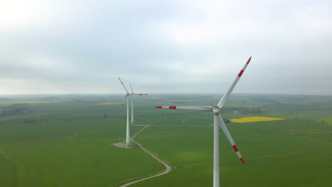 Schöne-Windmühlenturbinen-Auf-Grünen-Wiesen-Während-Des-Dunstigen-Morgens