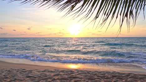 Sunset-at-tropical-paradise,-yellow-sun,-sandy-island-beach-and-palm-tree-shade,-full-frame-slow-motion