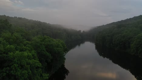 Narrow-forest-river-with-rising-fog-in-early-summer-morning,-aerial-view