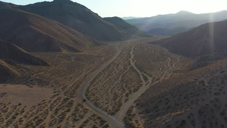 A-lone-car-drives-along-a-road-in-a-valley-between-hills-and-mountains-in-the-Mojave-Desert---aerial-view