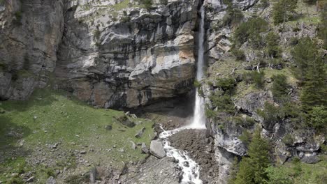 Ein-Aus-Der-Luft-Sichtbarer-Wasserfall,-Der-Hinter-Einem-Massiven-Felsen-Herunterstürzt-Und-Einen-Nebel-Aus-Spritzendem-Wasser-Erzeugt
