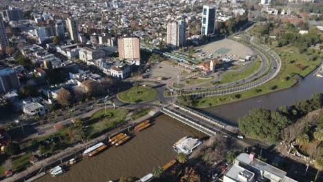 Aerial-flight-showing-Tigre-Cityscape-with-docking-ships-in-Primero-River-and-traffic-at-roundabout-during-sunset
