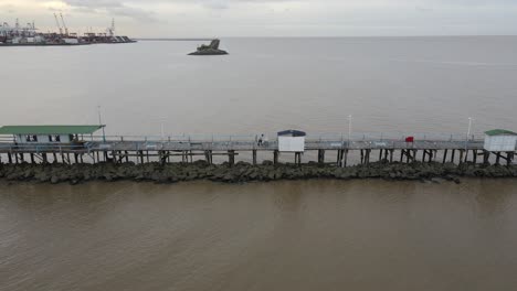Aerial-view-of-a-man-pushing-a-cart-on-a-wooden-pier-in-a-port-area-at-the-water's-edge