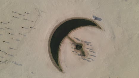 Aerial-view-of-the-Moon-Lake-in-Dubai,-Moon-Shape-Lake-is-in-the-middle-of-Al-Qudra-desert,-surrounded-by-golden-sand-dunes-in-the-United-Arab-Emirates